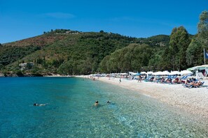 Uma praia com água cristalina, pessoas nadando e guarda-sóis na orla.