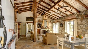 Un intérieur rustique avec des murs en pierre, un sol en pierre, un plafond en bois, une cheminée, un canapé, une table à manger avec des chaises et un téléviseur.