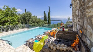 Une piscine avec des chaises longues, un mur en pierre et un barbecue.