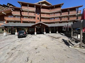 A multi-story building with balconies, a parking area, and a ski rental sign.