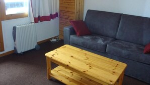 Une pièce chaleureuse avec un canapé gris, une table en bois, un radiateur et une carte accrochée au mur.