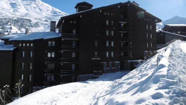 Un immeuble à plusieurs étages, doté d’une façade sombre, entouré d’un paysage enneigé et avec des montagnes en arrière-plan.
