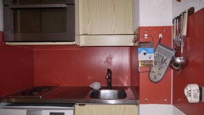 Une cuisine compacte équipée d’un four à micro-ondes, d’une cuisinière, d’un évier et de meubles de rangement en bois.