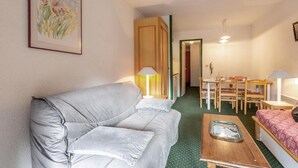 A compact hotel room with a grey sofa, a small dining table with chairs, a bed with a red cover, and a green carpet. - 90m from ski slopes, 4th floor, view mountain, balcony, 36m², Méribel-Mottaret (Méribel - Les Allues)