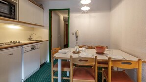 A compact kitchen with a microwave, stove, and sink. There is a dining table with chairs and a hanging light fixture. - 90m from ski slopes, 4th floor, view mountain, balcony, 36m², Méribel-Mottaret (Méribel - Les Allues)