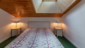 A bedroom with a sloped ceiling, a skylight, a bed with a patterned bedspread, two bedside tables with lamps, and green carpeting. - 90m from ski slopes, 4th floor, view mountain, balcony, 36m², Méribel-Mottaret (Méribel - Les Allues)