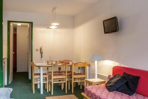A compact room with a dining table and chairs, a red sofa, a TV mounted on the wall, and a door leading to another room. - 300m from resort center, 4th floor, view mountain, balcony, 36m², Méribel-Mottaret (Méribel - Les Allues)