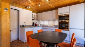 A modern kitchen with white cabinets, a black dining table with orange chairs, and a wooden ceiling. - 130m from ski slopes, 1st floor, view resort, balcony, ski locker, 44m², Méribel-Mottaret (Méribel - Les Allues)