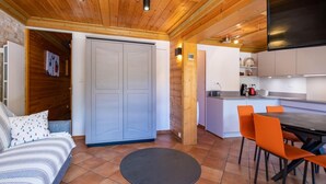 A cozy living area with a sofa, a round table, and orange chairs. There's a kitchen with a TV and a dining table. - 130m from ski slopes, 1st floor, view resort, balcony, ski locker, 44m², Méribel-Mottaret (Méribel - Les Allues)