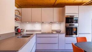 A modern kitchen with white cabinets, a built-in oven, and a dining area with orange chairs. - 130m from ski slopes, 1st floor, view resort, balcony, ski locker, 44m², Méribel-Mottaret (Méribel - Les Allues)
