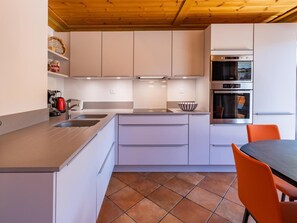 A modern kitchen with white cabinets, a built-in oven, and a dining area with orange chairs. - 300m from resort center, 1st floor, view resort, balcony, ski locker, 44m², Méribel-Mottaret (Méribel - Les Allues)