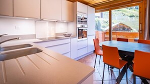 A modern kitchen with white cabinets, a large island, and a dining area with orange chairs. - 130m from ski slopes, 1st floor, view resort, balcony, ski locker, 44m², Méribel-Mottaret (Méribel - Les Allues)