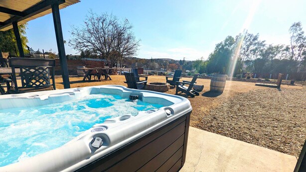 A hot tub with a wooden exterior, surrounded by outdoor furniture and a gravel area. - Pool Table + Firepit + BBQ | Eastside Paso Wine Country | Casa Merlot (Paso Robles)