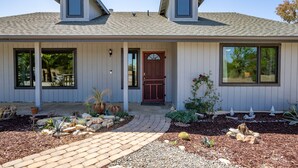 A single-story house with a red door, two windows on the front, and a small porch area with potted plants. - Pool Table + Firepit + BBQ | Eastside Paso Wine Country | Casa Merlot (Paso Robles)