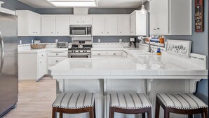 A modern kitchen with white cabinetry, a central island with stools, a microwave, a stove, and a coffee maker. - Pool Table + Firepit + BBQ | Eastside Paso Wine Country | Casa Merlot (Paso Robles)