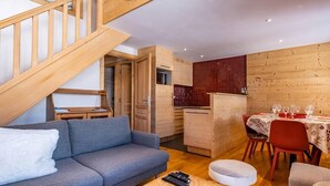 Ein gemütliches Zimmer mit einer Holztreppe, einem grauen Sofa, einem Esstisch für vier Personen und einer Küchenzeile.