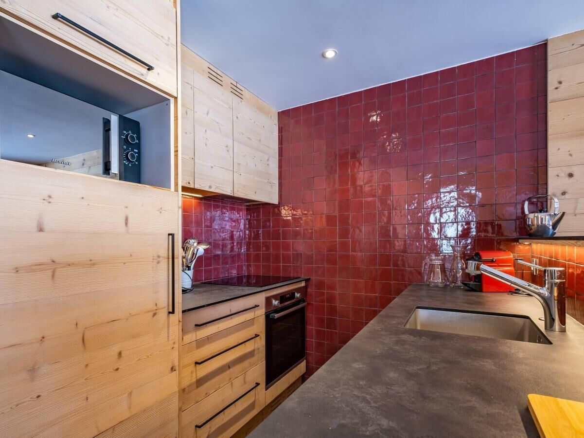 A modern kitchen with wooden cabinetry, a red-tiled backsplash, and stainless steel appliances.