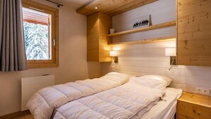 Ein Schlafzimmer mit Bett, Nachttischen, einem Fenster mit Vorhängen und einer Holzbalkendecke.