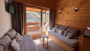 Una habitación de cabaña de madera con sofá, una mesita y un televisor montado en la pared.