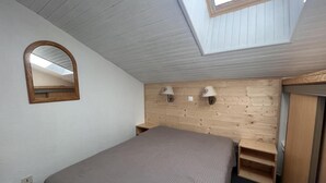 Un dormitorio con tragaluz, una cama, cabecera de madera y un espejo.