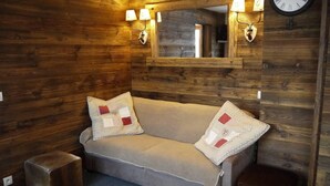 Ein gemütliches Zimmer mit Holzwänden, einer Couch mit zwei Zierkissen, einer Wanduhr und zwei Wandleuchten.