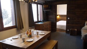 Ein gemütliches Zimmer mit Holztisch gedeckt für das Frühstück, einem Bett mit hölzernem Kopfteil und einem Fernseher auf einer Kommode.