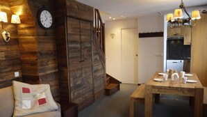 Ein gemütlicher Raum mit Holzwand, einer Couch mit Zierkissen, einem Esstisch für vier Personen und einer Treppe, die in eine andere Ebene führt.