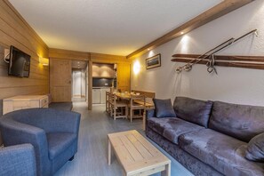 Una sala de estar acogedora con sofá, sillón y mesa de centro de madera. Se ve un comedor con mesa y sillas al fondo.