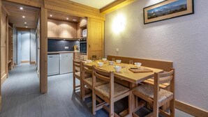 A wooden dining table with chairs, a kitchen area with wooden cabinets, and a framed picture on the wall. - 80m from ski lifts, 4th floor, balcony, ski locker, 46m², Méribel-Mottaret (Méribel - Les Allues)