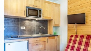 Kompakti keittiö, jossa on puiset kaapit, mikroaaltouuni, pesuallas ja Bosch-merkkinen jääkaappi.
