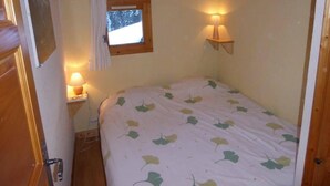 Ein gemütliches Schlafzimmer mit einem Bett, zwei Nachttischlampen, einem Fenster mit Blick auf eine verschneite Landschaft und einer Holzbalkendecke.