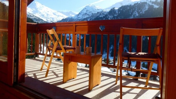Eine Holzterrasse mit Tisch und Stühlen mit Blick auf eine verschneite Berglandschaft.