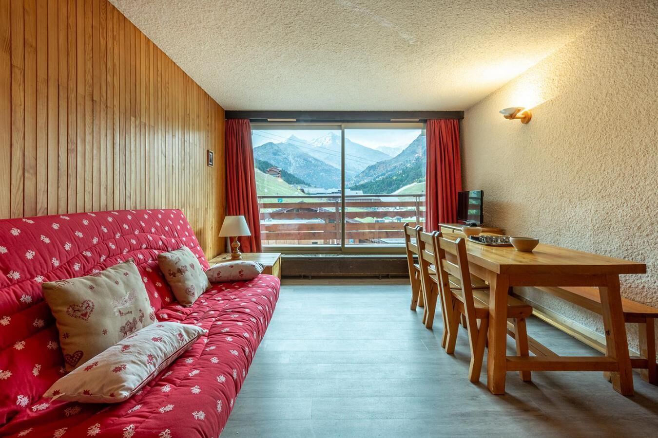 Ein gemütliches Zimmer mit einem roten Sofa, einem Holzesstisch und Bergblick durch ein großes Fenster.