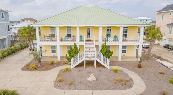 A two-story building with a green roof, a central staircase, and a small garden area. - The Big Yellow Beach House | Gulf Views, Private Pool - Sleeps 17 (Pensacola Beach)