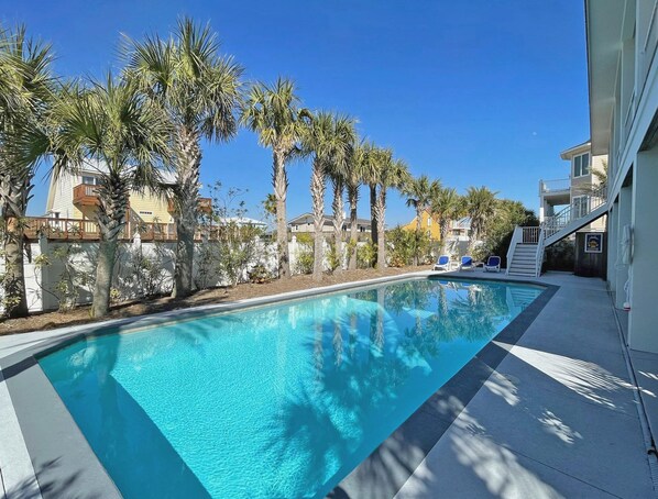 Relax by the serene pool surrounded by lush palm trees and lounge chairs.