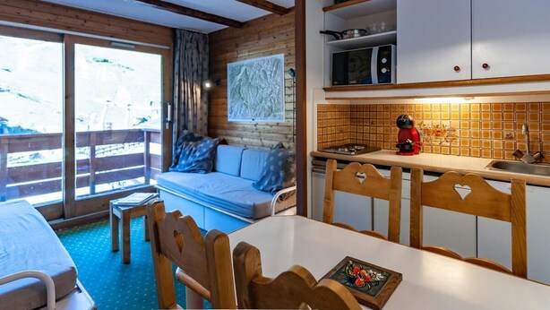 Una habitación acogedora con techo de madera, un sofá con cojines, una mesa de comedor con sillas, una zona de cocina con microondas y un ventanal con vistas.