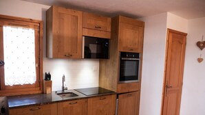 A compact kitchen with wooden cabinets, a built-in microwave, oven, and sink. - 150m from shops, view parking, balcony, tv, 44m², Méribel-Mottaret (Méribel - Les Allues)