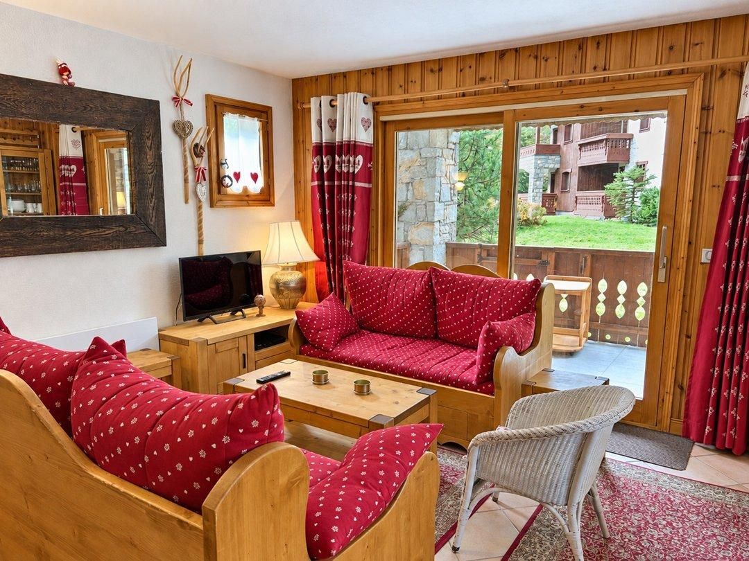 A cozy living room with a red sofa, wooden furniture, a television, and a large window with curtains.