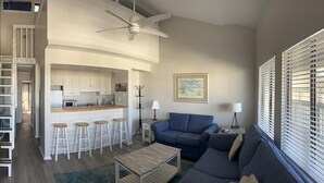 A spacious living area with a high ceiling, a kitchen with white cabinets, a blue sofa, and a dining area with stools.