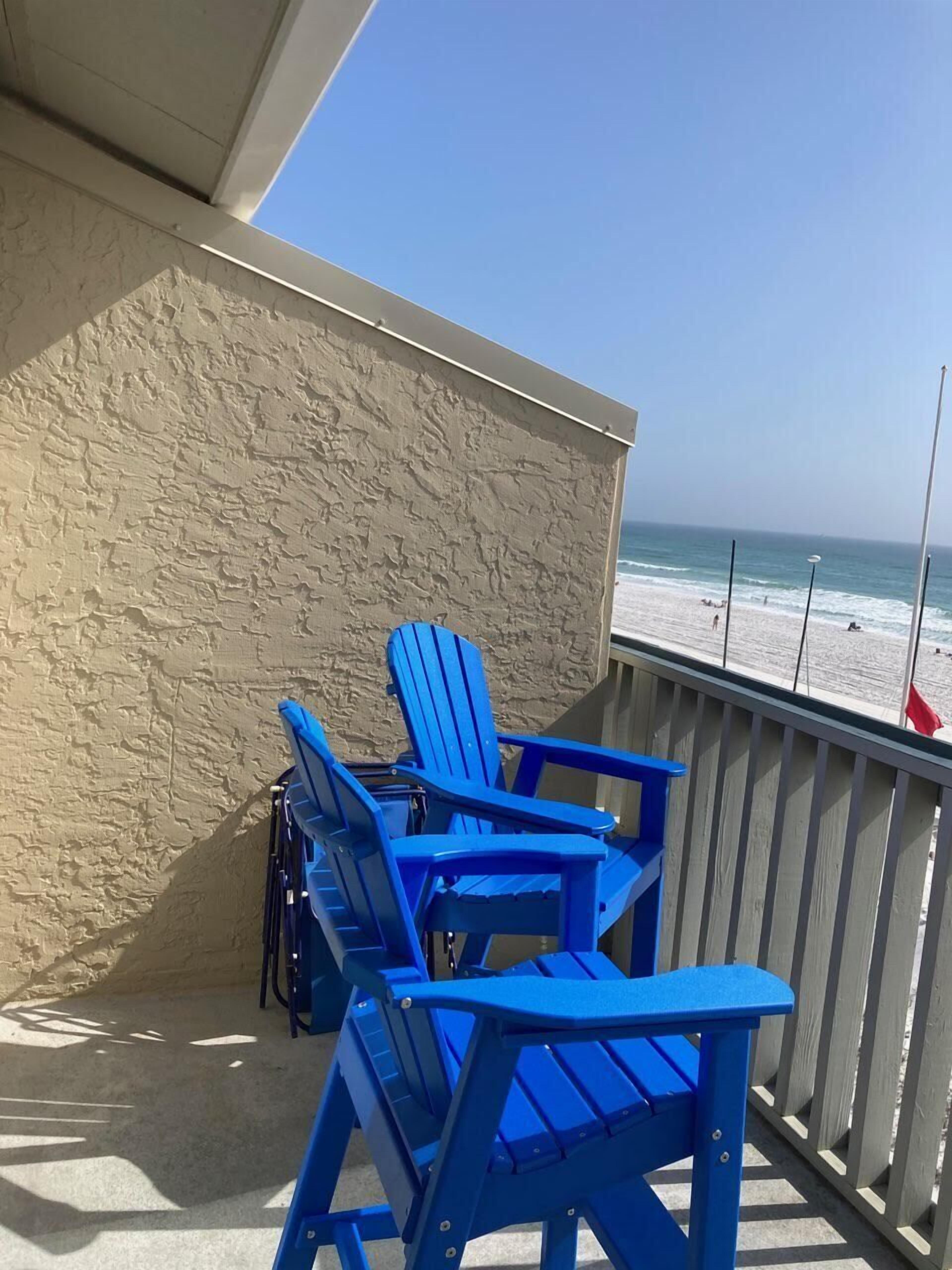 A balcony with blue Adirondack chairs overlooking a beach.