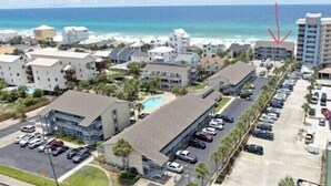 A coastal residential area with a row of modern buildings, a parking lot, and a view of the ocean.