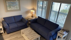 A living room with two dark blue sofas, a wooden coffee table, a lamp, and a framed picture on the wall.