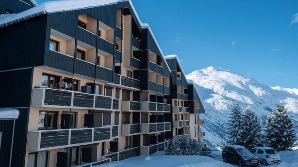 Un hôtel à plusieurs étages doté de balcons, avec une montagne enneigée en arrière-plan et des voitures garées.