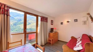 Une chambre à coucher avec un lit, une commode en bois, un bureau avec une lampe et une vue sur l’extérieur.