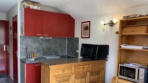 Une cuisine de taille réduite avec des placards rouges, un four à micro-ondes et une table en bois.
