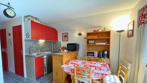 Une cuisine compacte avec des meubles de rangement rouges, une table à manger en bois avec des chaises et un petit îlot central doté d’un évier.