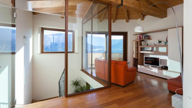 Un salon moderne avec un plafond en bois, de grandes portes-fenêtres coulissantes, un canapé rouge et un téléviseur posé sur un meuble blanc.