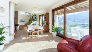 Un vaste espace de vie comprenant une table à manger, un canapé en cuir rouge et de grandes portes-fenêtres coulissantes donnant sur une vue imprenable sur les montagnes.