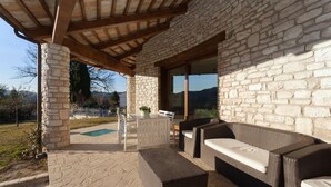 Une terrasse extérieure avec des murs en pierre, une pergola en bois, des meubles en osier et une vue sur le paysage.