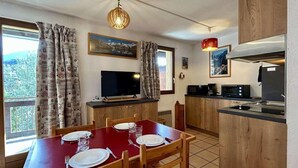 Un comedor con una mesa roja para cuatro, armarios de madera, un televisor y una zona de cocina con microondas y tostadora.